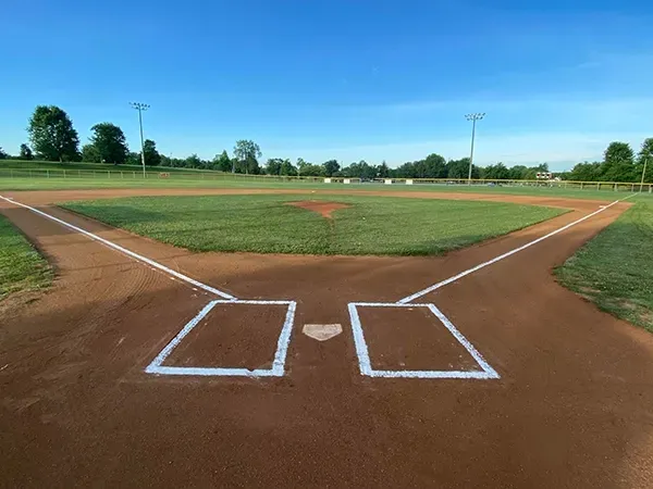 Baseball field with dirt infield, green outfield, and clear blue sky.