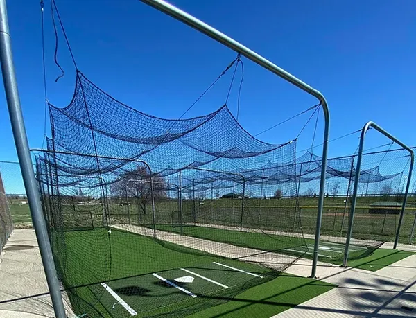 Baseball batting cage with green turf, black netting, and metal frame, against a blue sky.