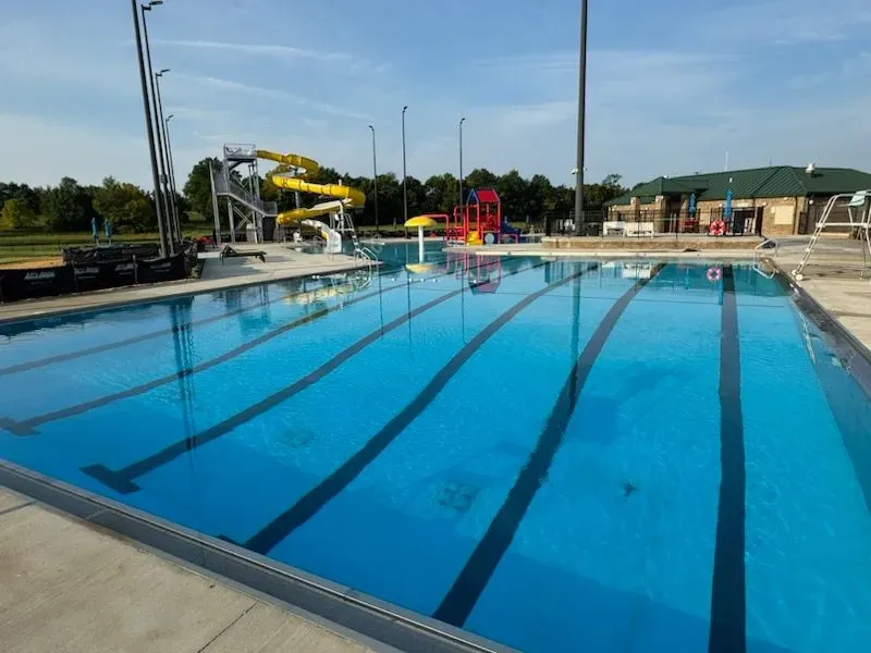 Empty outdoor swimming pool with lanes, a yellow water slide, and a building in the background.