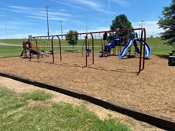 A playground with a slide and swings in a park on a sunny day.