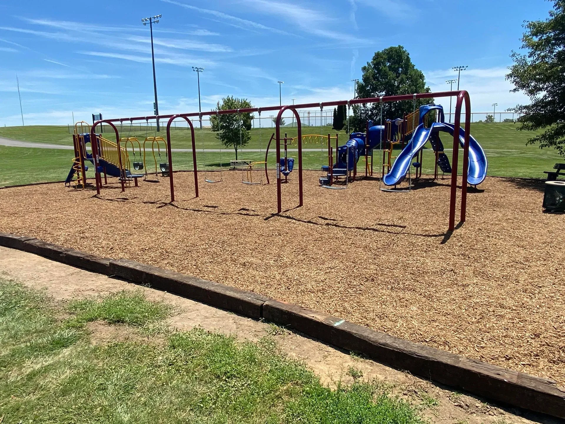 Playground with swings, slides, and wood chip ground cover, under a bright blue sky.