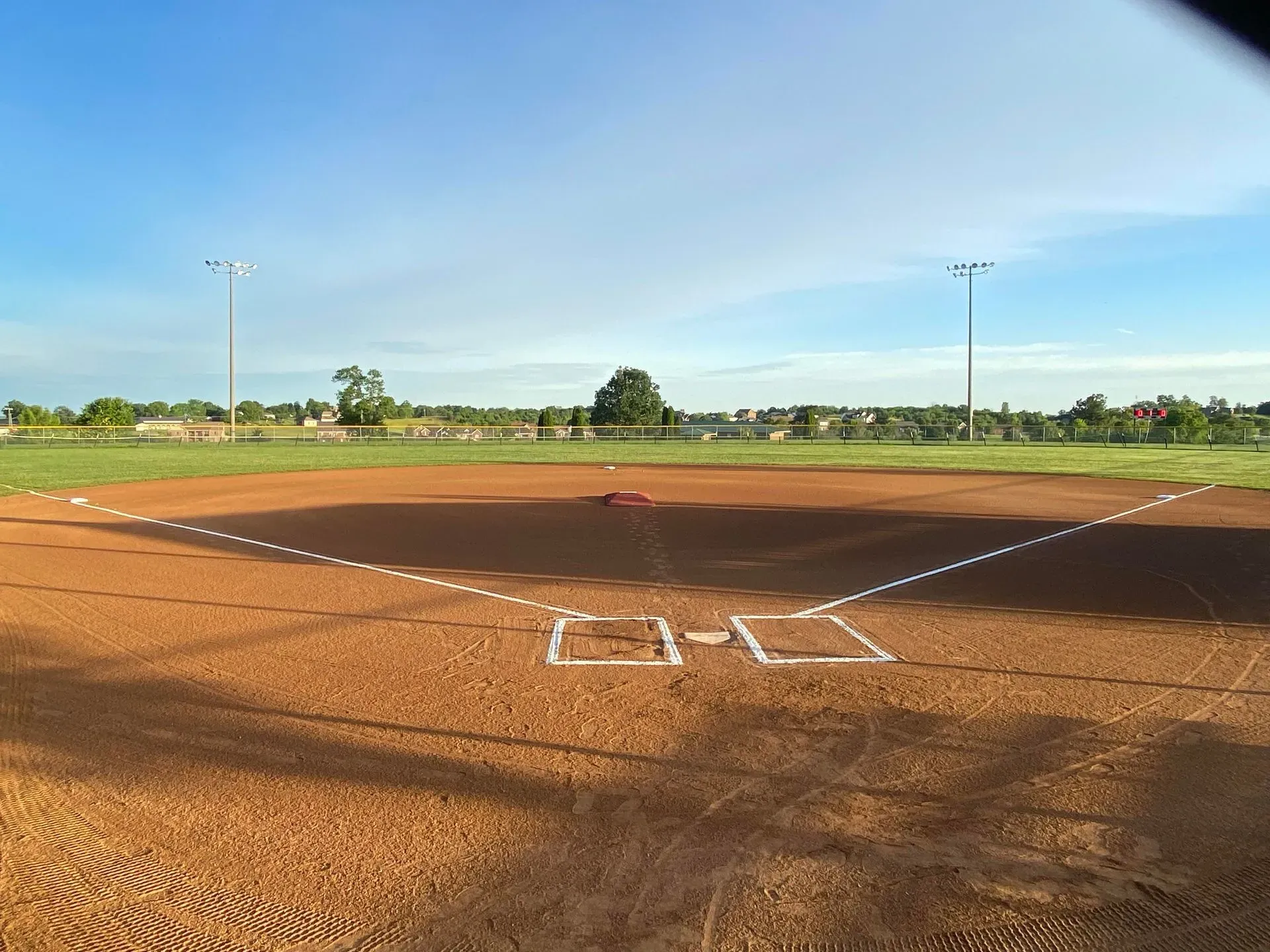 Empty baseball field with dirt infield and bright blue sky.