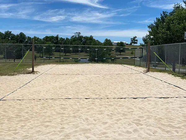 Empty sand volleyball court with net, trees, and blue sky.