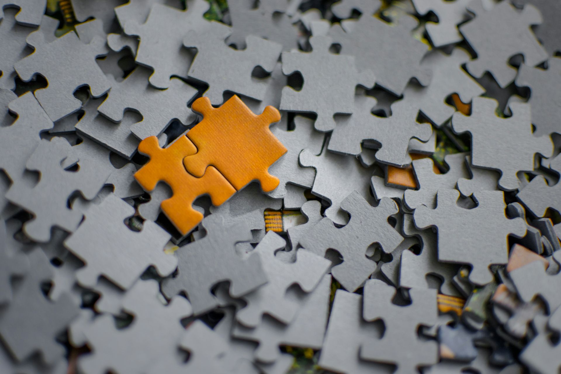 Orange puzzle piece on a scattered pile of gray puzzle pieces.