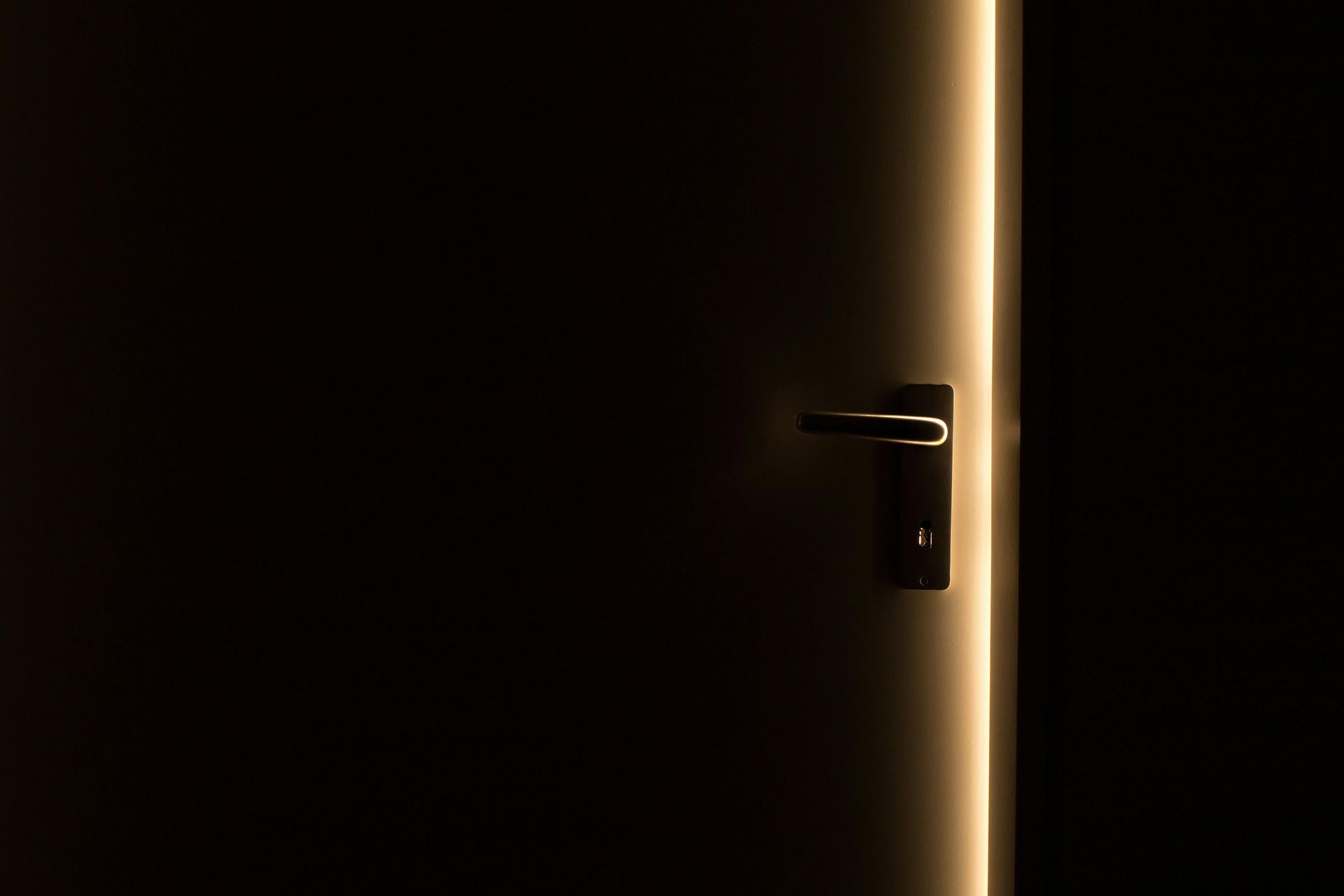 Dark door slightly ajar, bright light outlining the edge, handle visible.