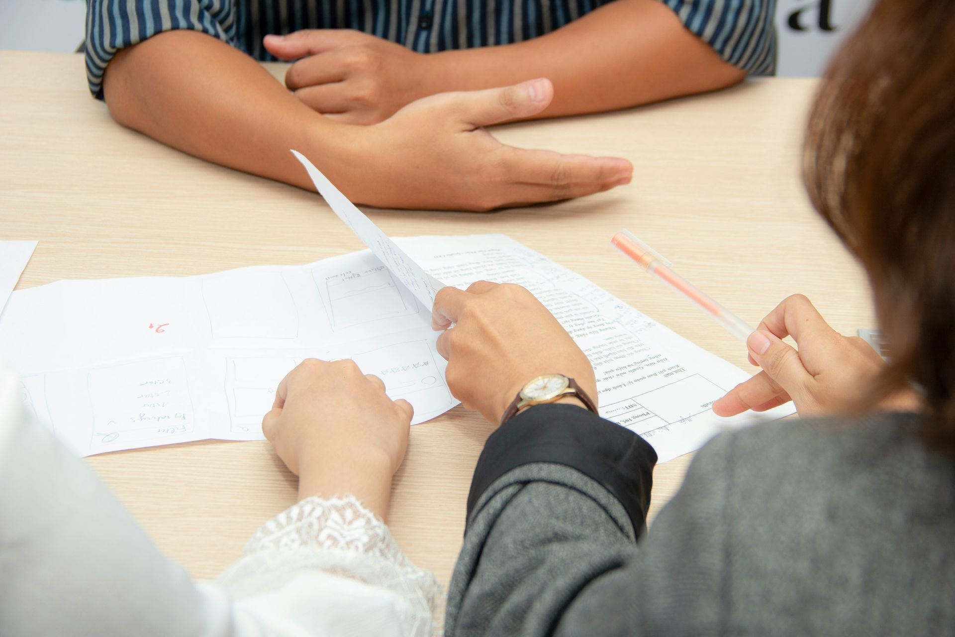 Hands examining paperwork at a table; person in blue shirt gestures.