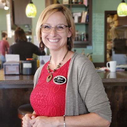 A woman wearing glasses and a red top is smiling in a restaurant