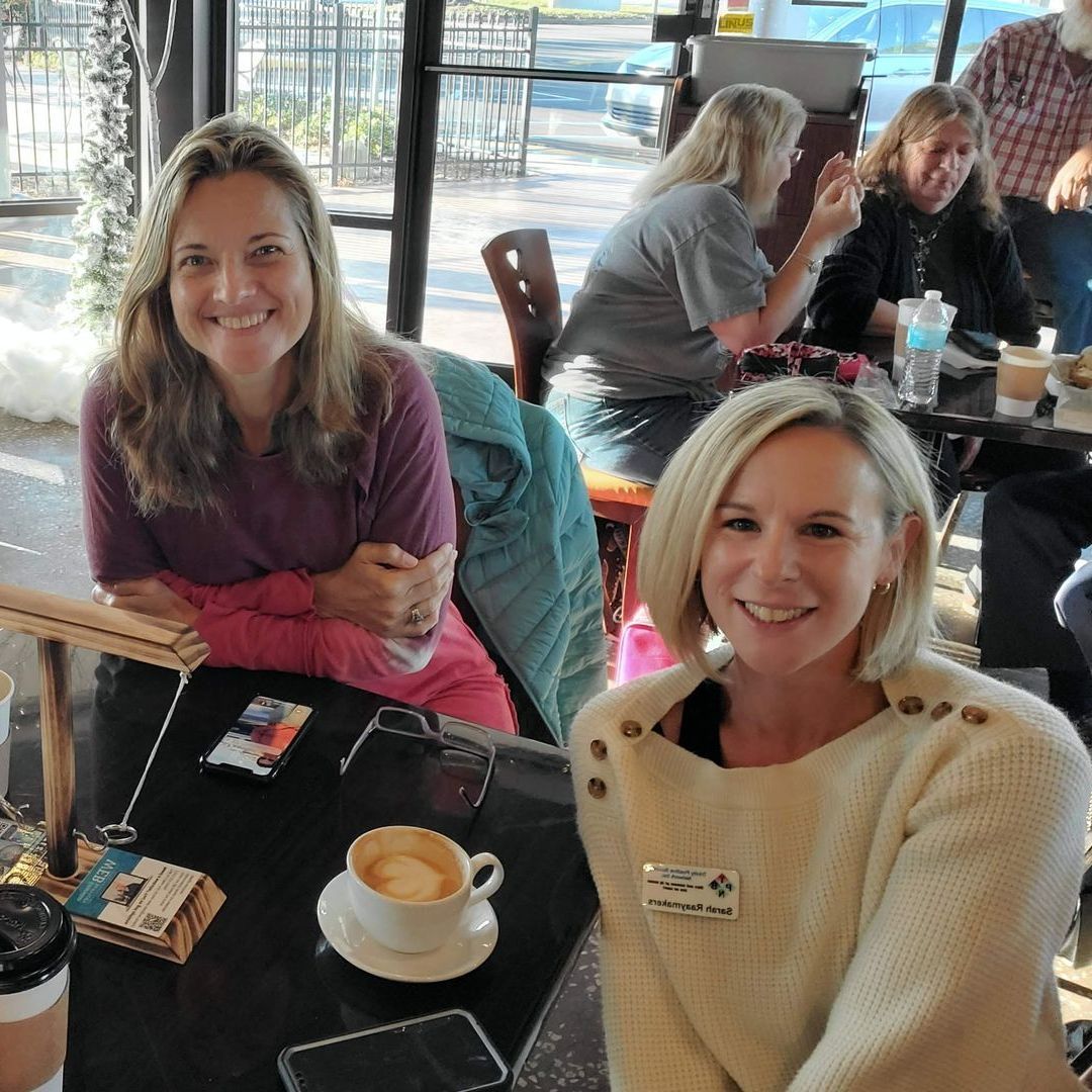 Two women are sitting at a table with a cup of coffee
