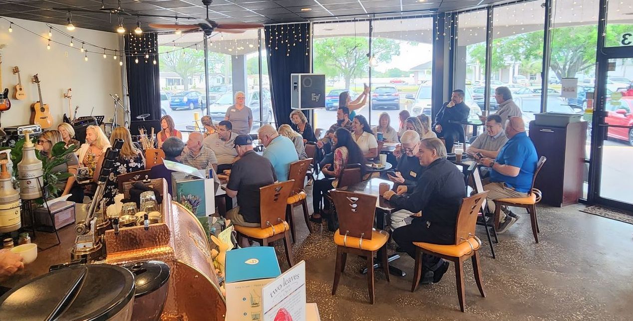 Candid group photo of 50 business owners sitting around various tables at a coffee shop