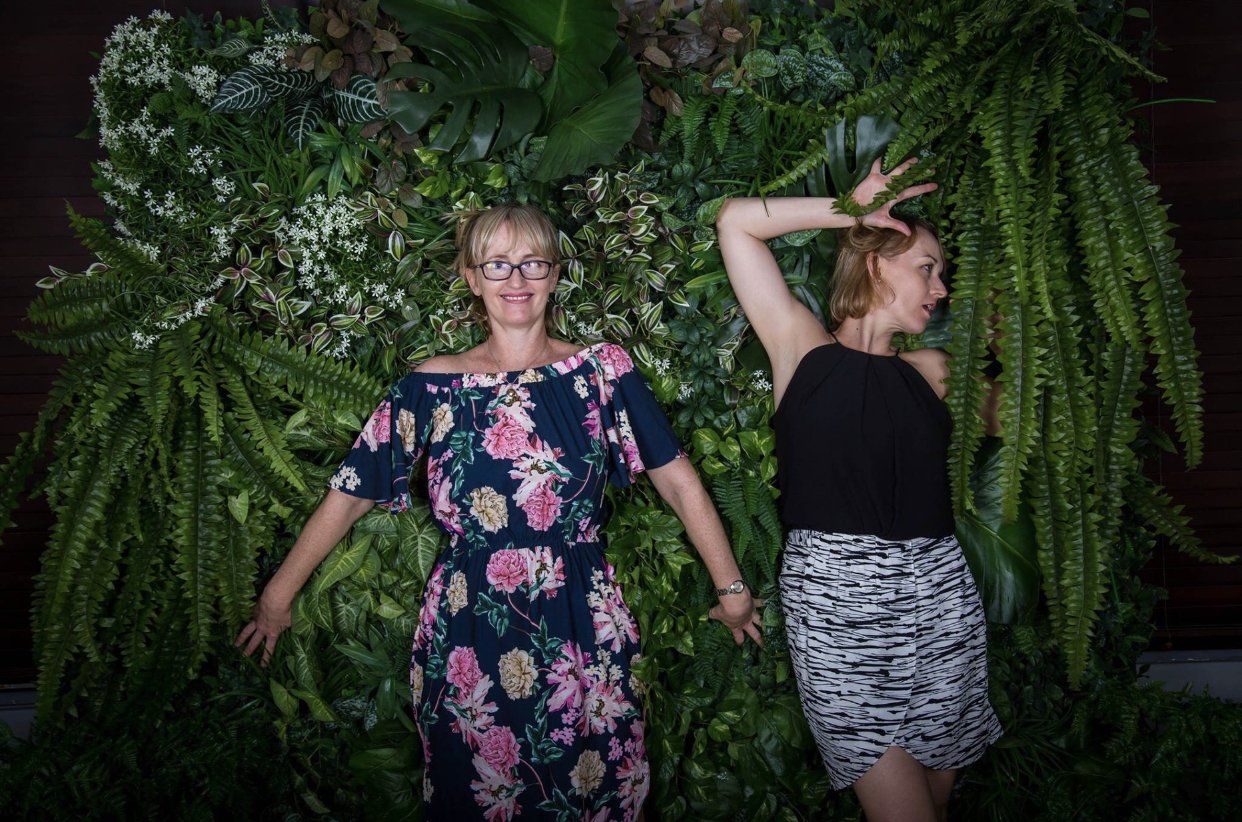 Darwin flower shop team relaxing against a lush green plant wall, symbolizing their connection to nature.