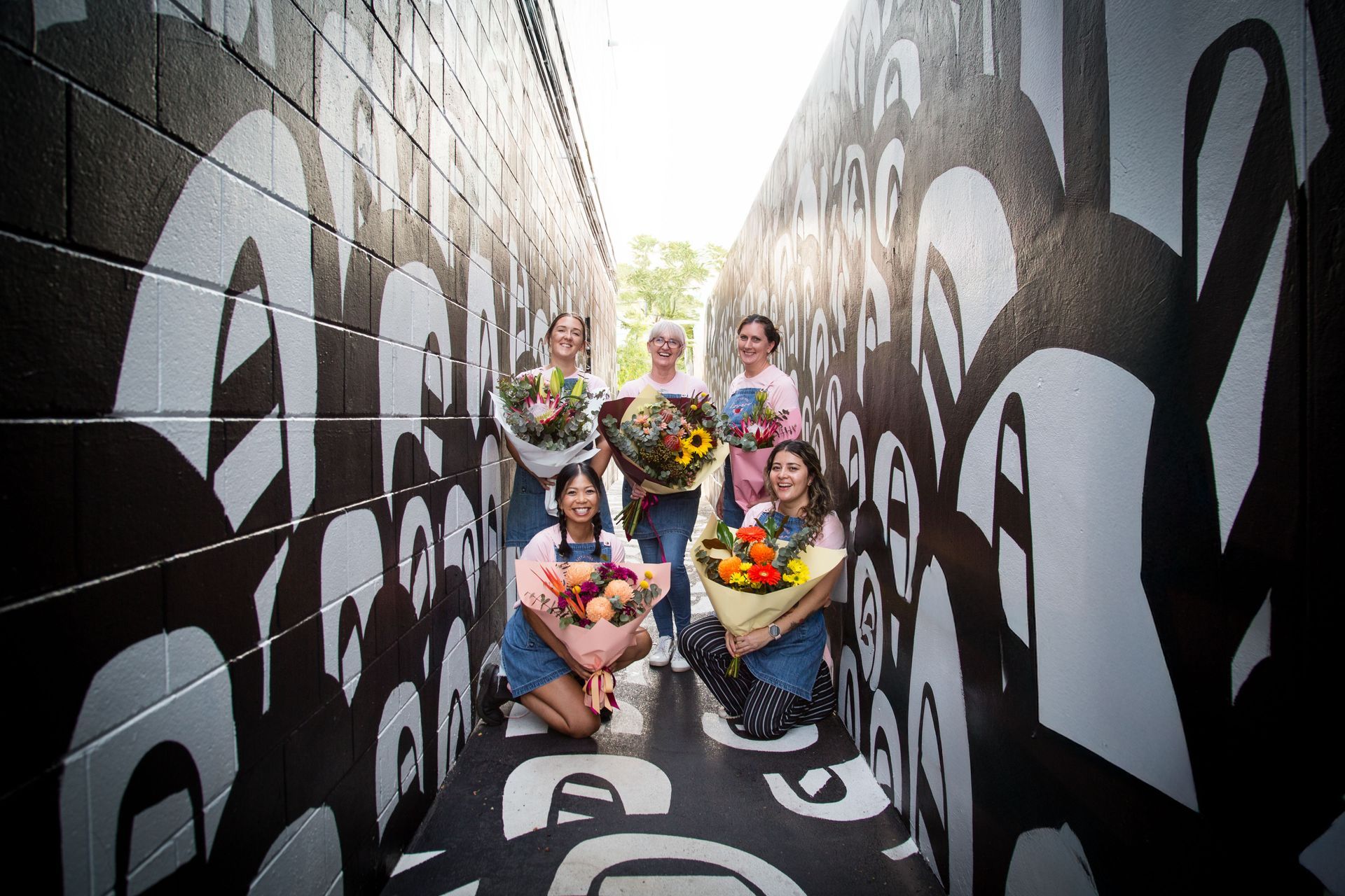 Darwin flower shop's team, all smiles, proudly displaying purple blooms, symbolizing joy and togetherness.