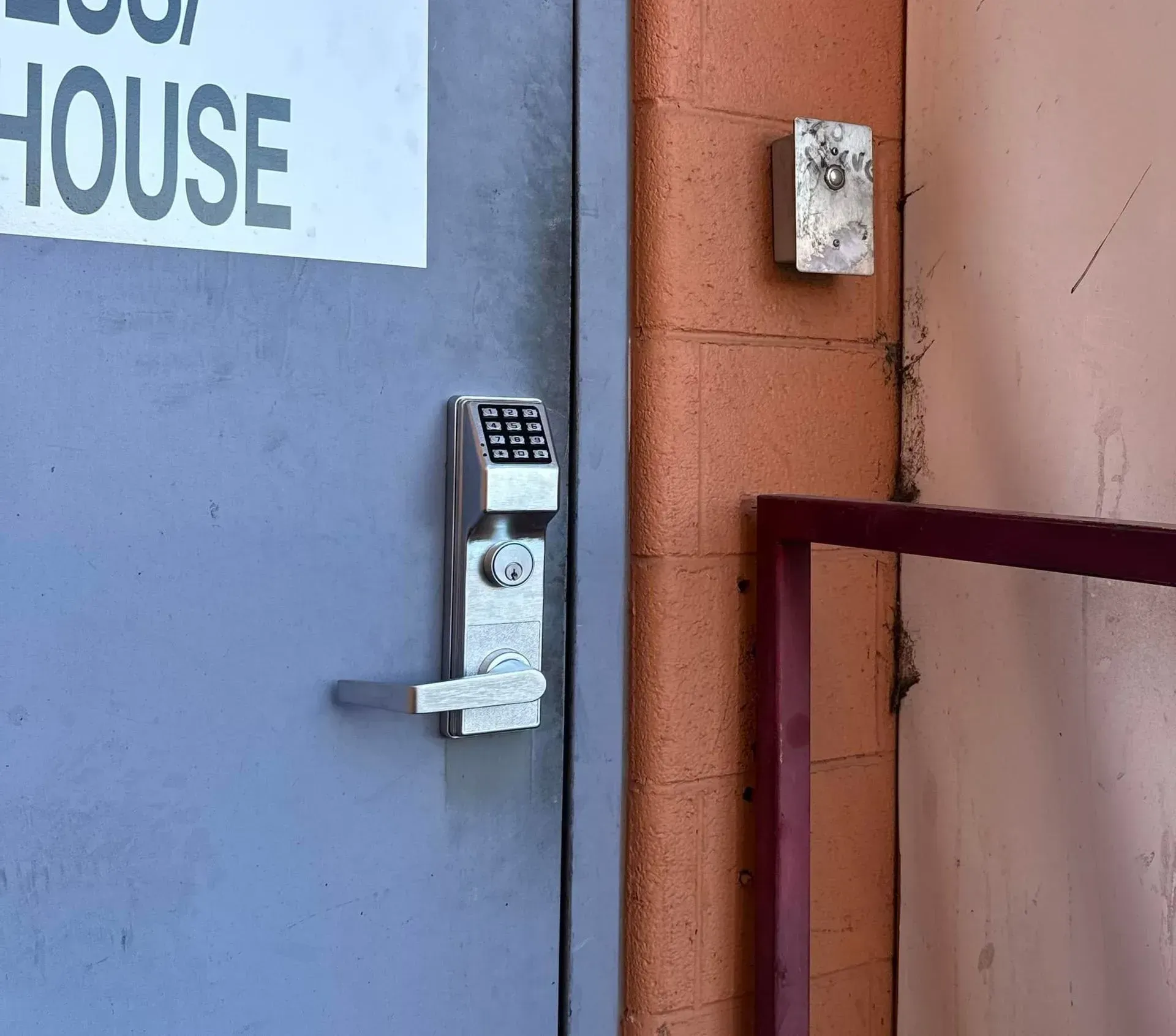 Keypad lock on a blue door beside a red wall and railing