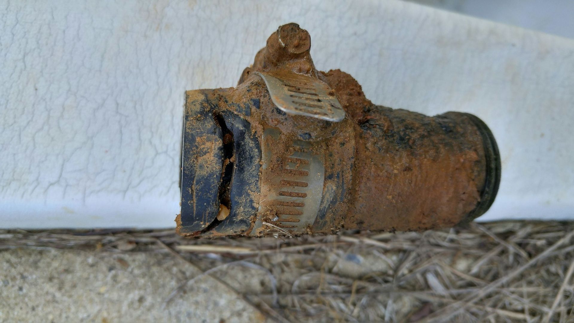 A rusty pipe is sitting on top of a pile of hay.