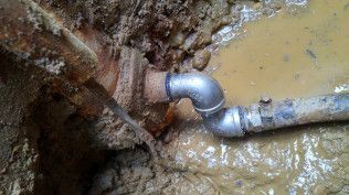 A pipe is stuck in the mud in a hole.