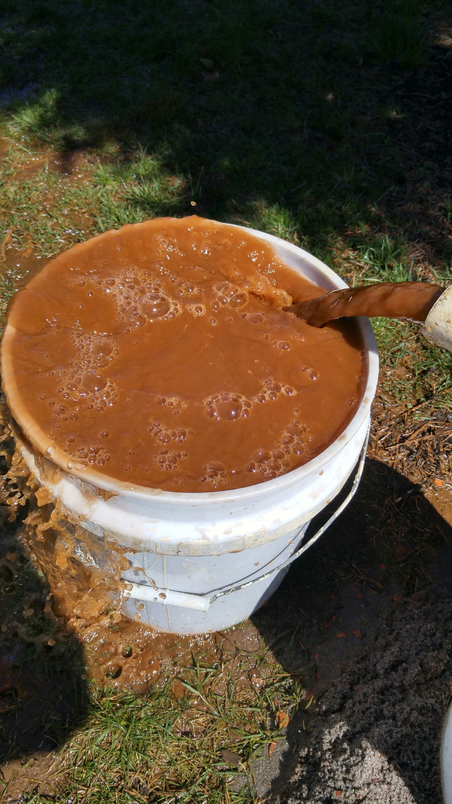 A bucket of brown liquid with a wooden spoon in it.