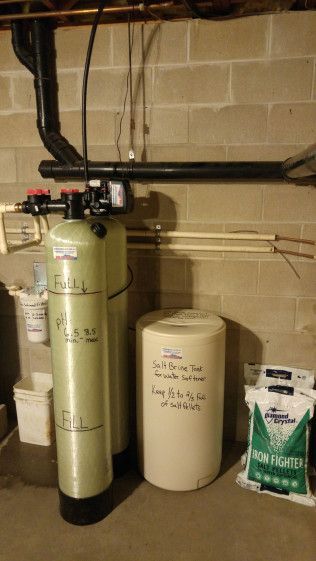 A water treatment system is sitting in a basement next to a brick wall.