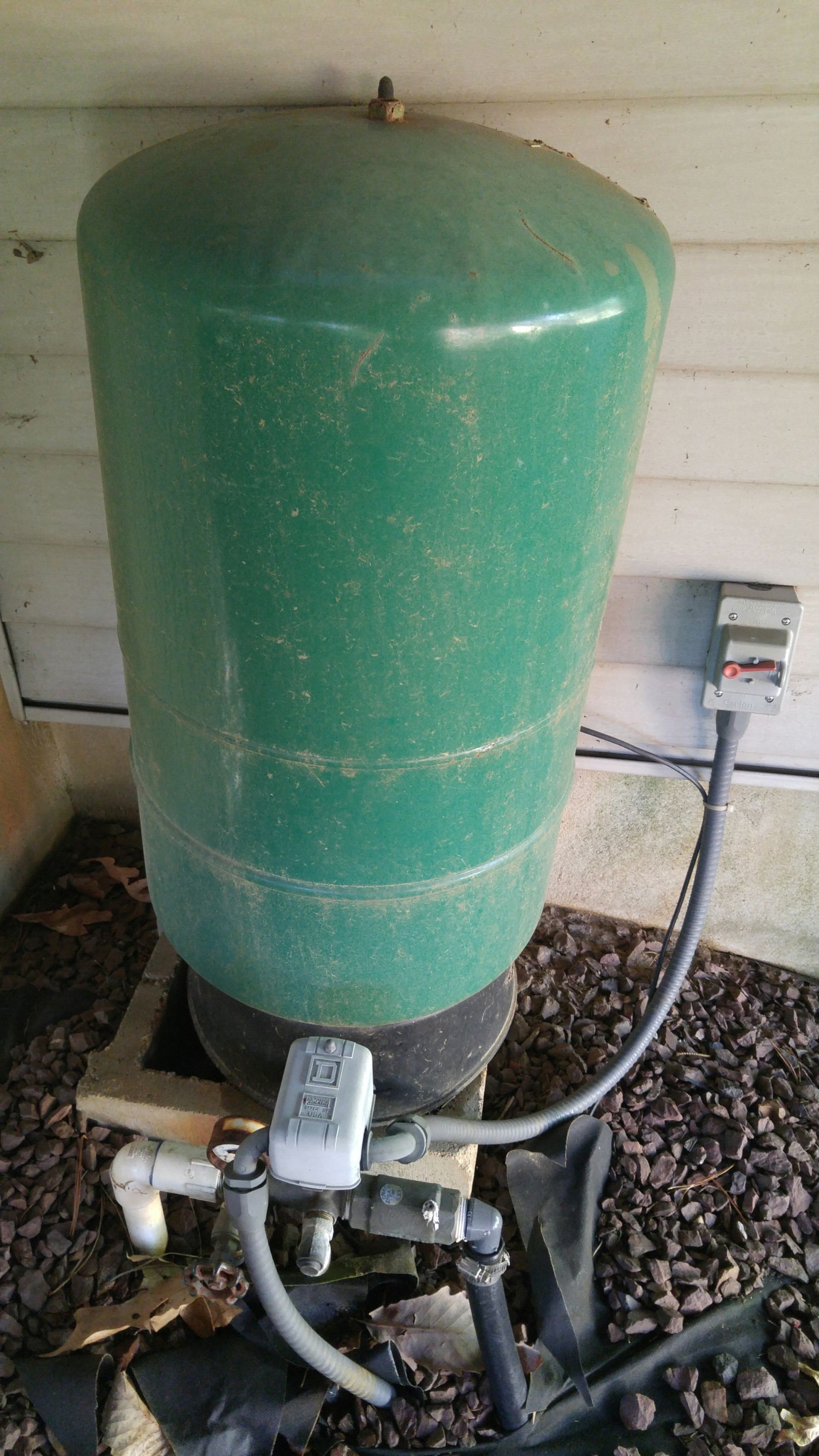 A green water tank is sitting on the ground next to a house.