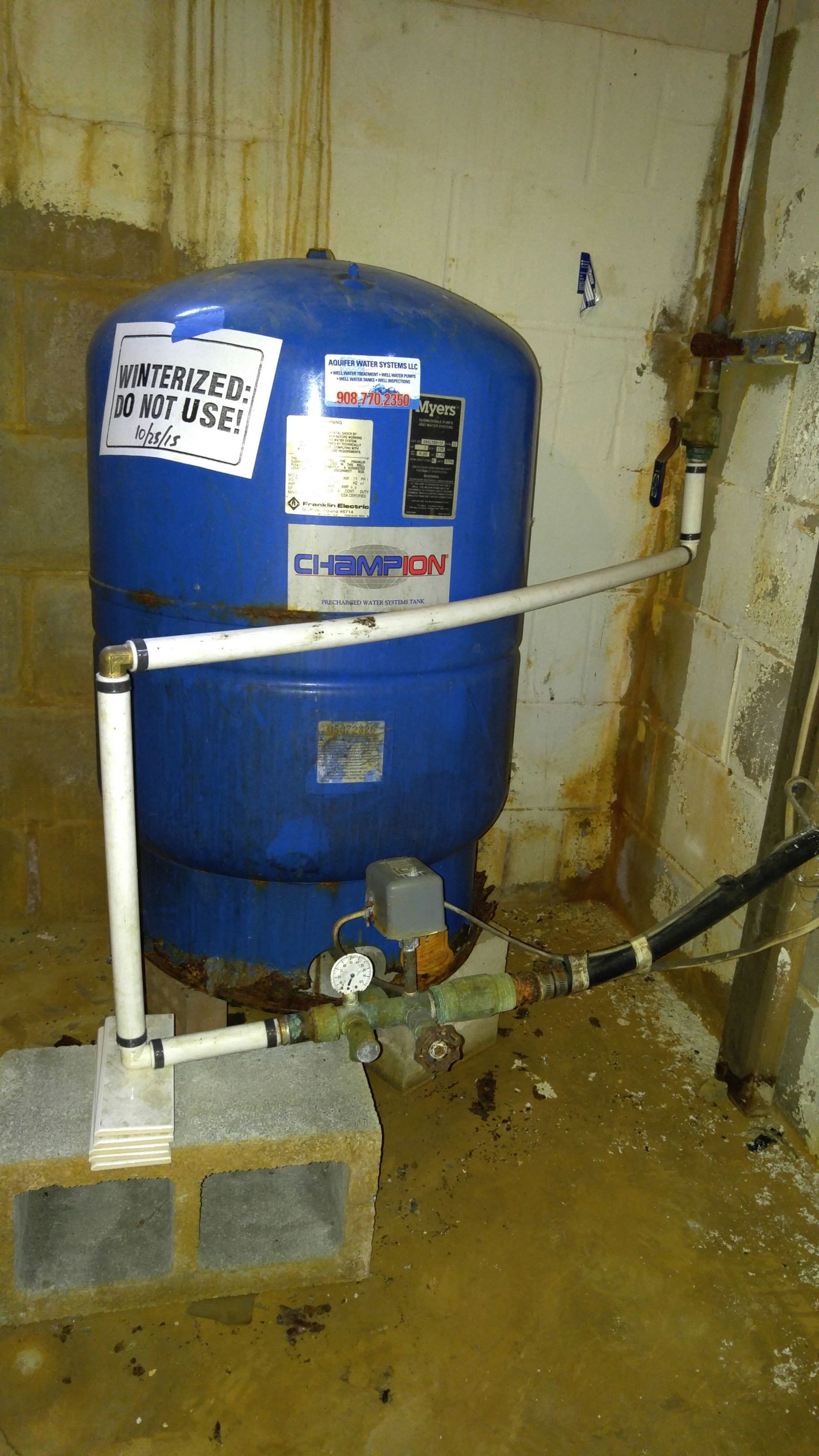 A blue water tank is sitting in a basement next to a wall.