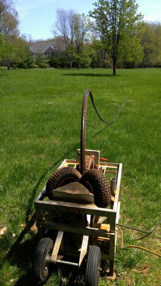 An old water pump is sitting on top of a cart in a grassy field.
