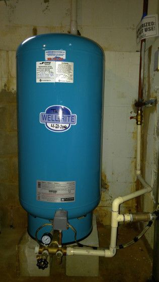A blue water heater is sitting in a room next to pipes.