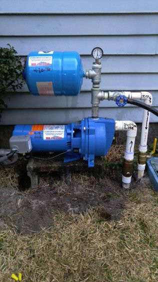 A blue water pump is sitting on the ground next to a house.