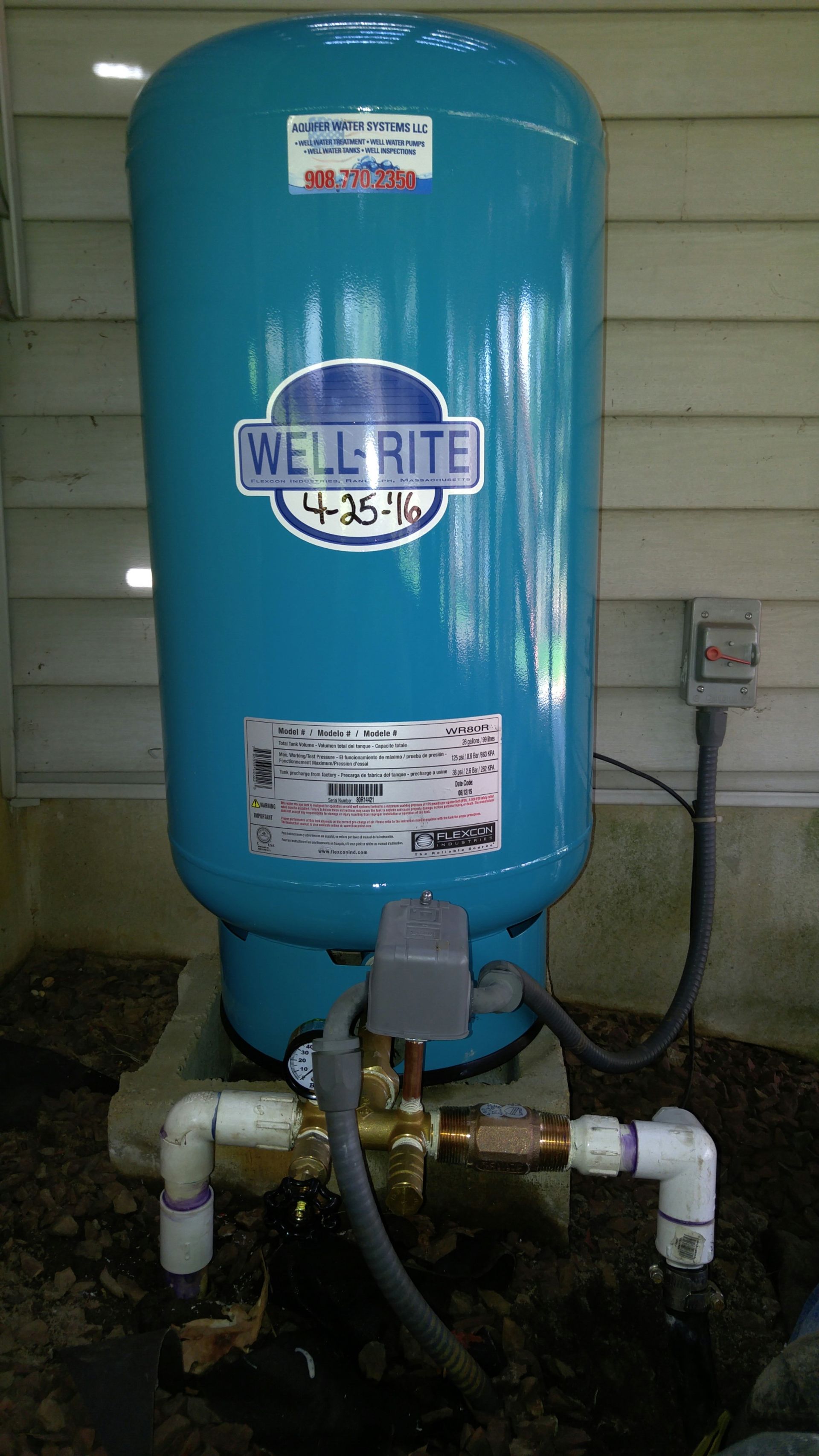 A blue water tank is sitting on the ground next to a wall.
