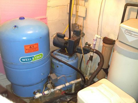 A well tank is sitting next to a water pump in a room.