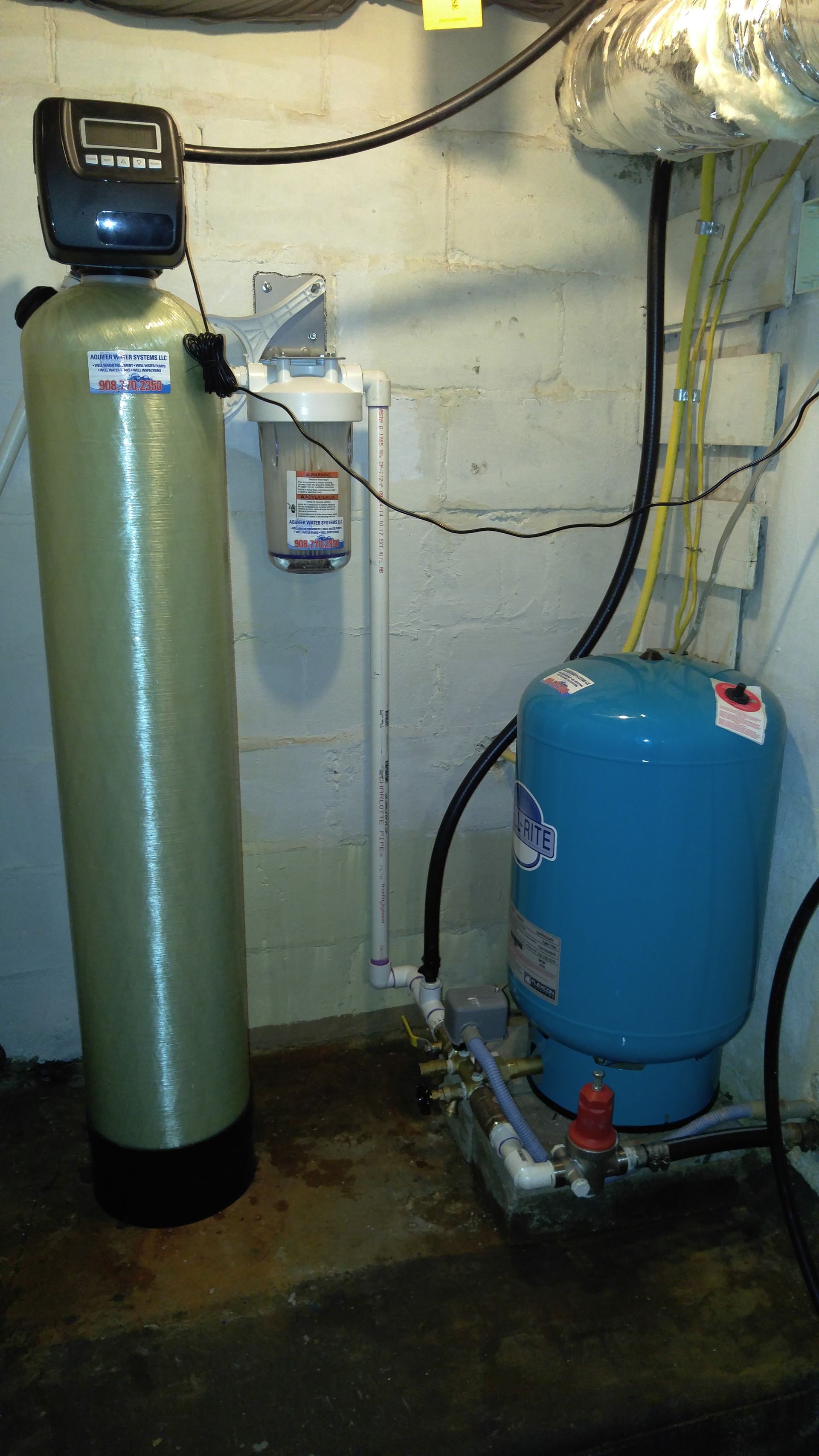 A water filter is sitting next to a water tank in a basement.