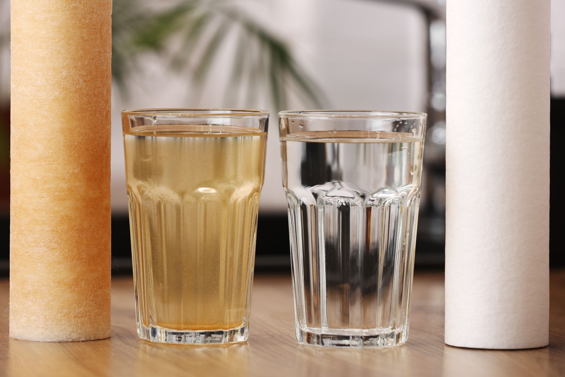 Two glasses of water are sitting on a wooden table next to a filter.