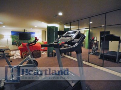 A treadmill in a basement with a heartland logo on the wall