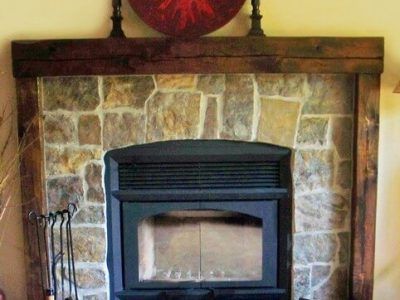 A fireplace with a stone wall and a wooden mantle.