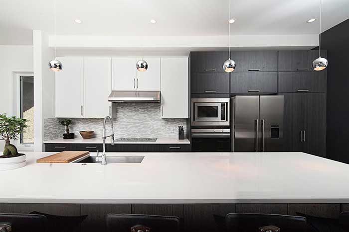 A kitchen with black and white cabinets , a stainless steel refrigerator , a sink , and a large island.