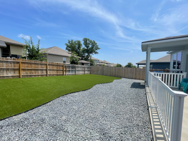 A gravel driveway leading to a house with a fence and grass.