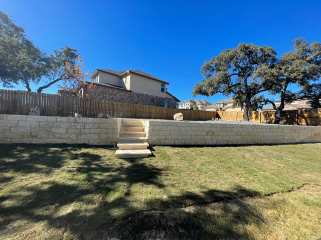 A backyard with a stone wall and stairs leading up to a house.