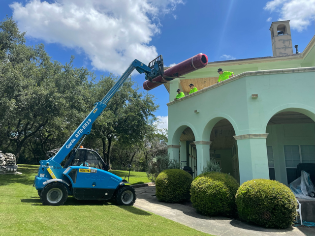 A crane is lifting a large pipe on top of a building.
