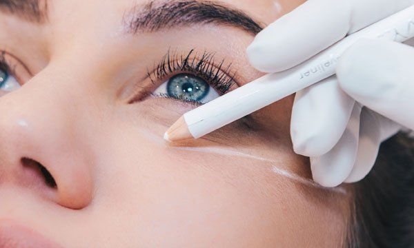 A woman is getting her eyebrows drawn with a pencil.