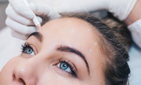A woman is getting a tattoo on her eyebrows.
