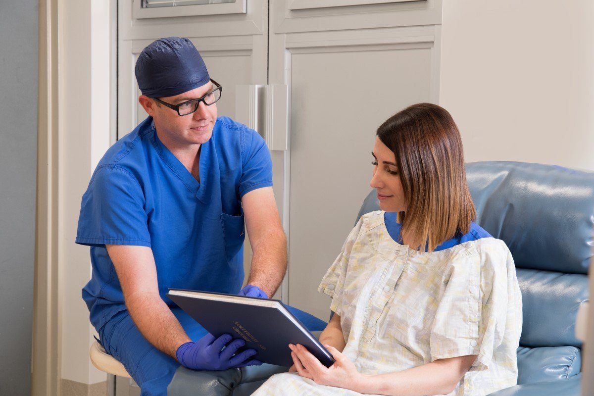 A doctor is talking to a patient in a hospital gown while looking at a tablet.