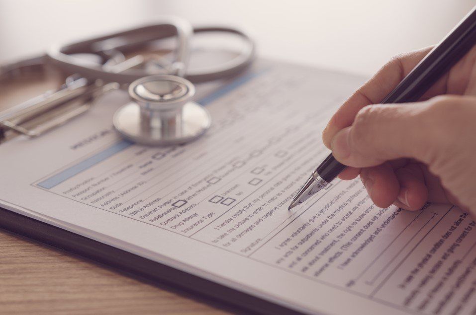 A person is writing on a clipboard with a pen next to a stethoscope.