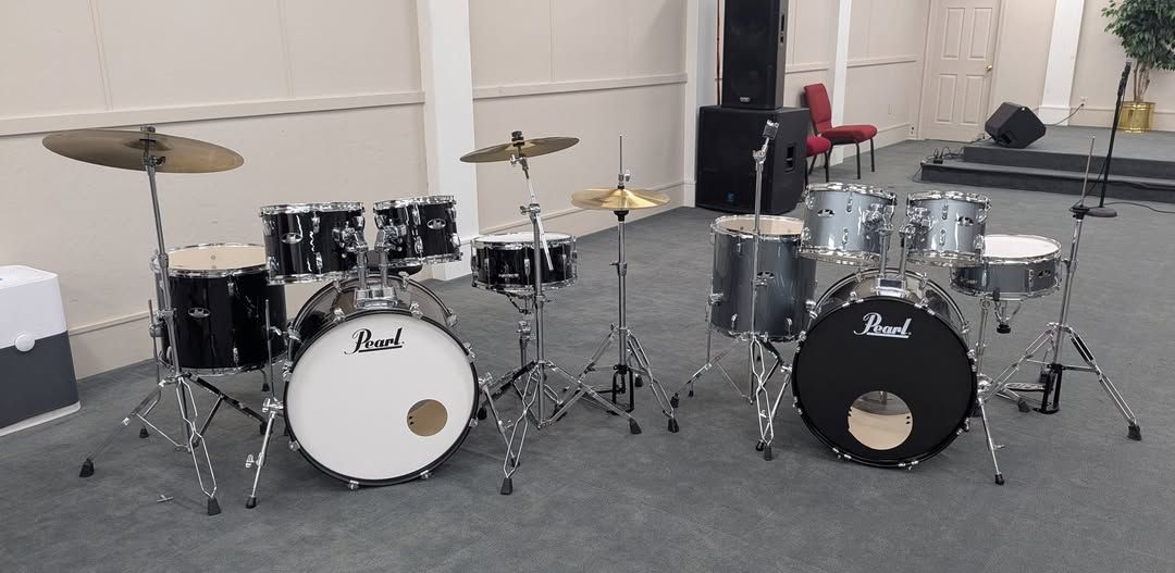 Two drum sets in a room. One with a white bass drum, the other with a black.