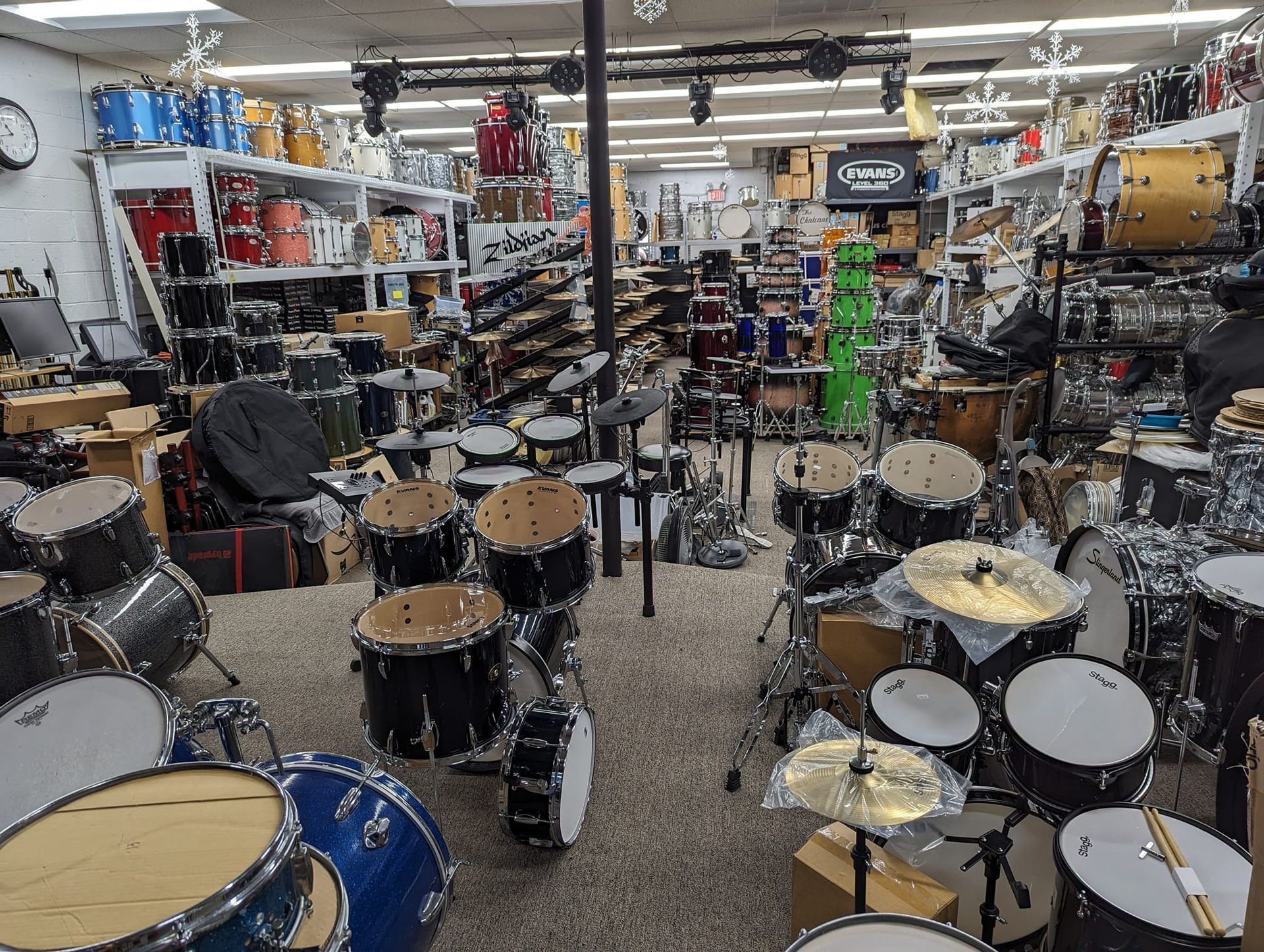 A cluttered music store interior filled with drums, cymbals, and equipment.