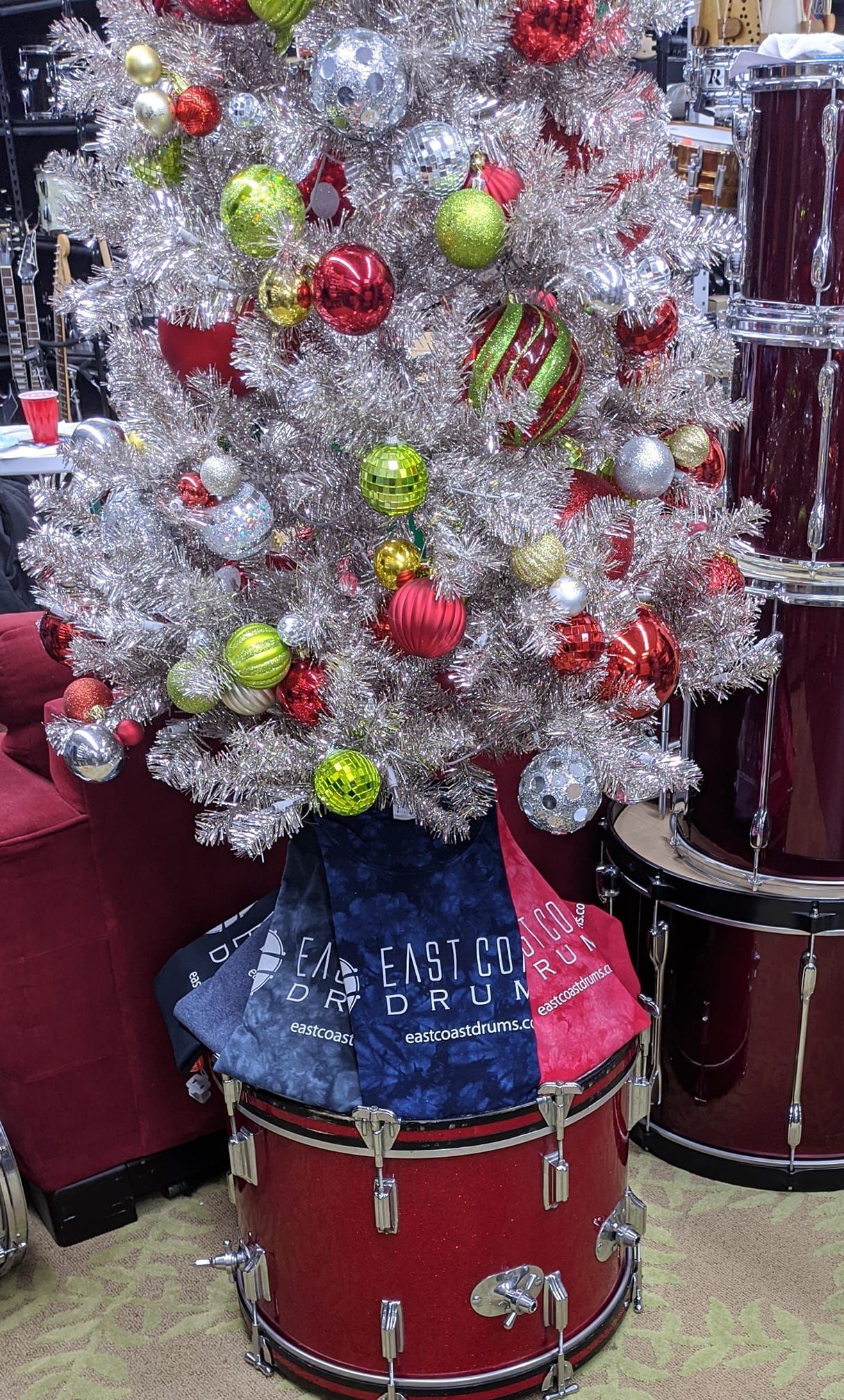 Silver Christmas tree decorated with ornaments, on top of a red drum.