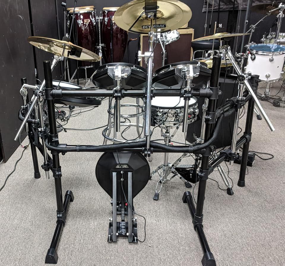 Electronic drum kit set up in a store, other drums visible in the background. Black, silver, and gold.