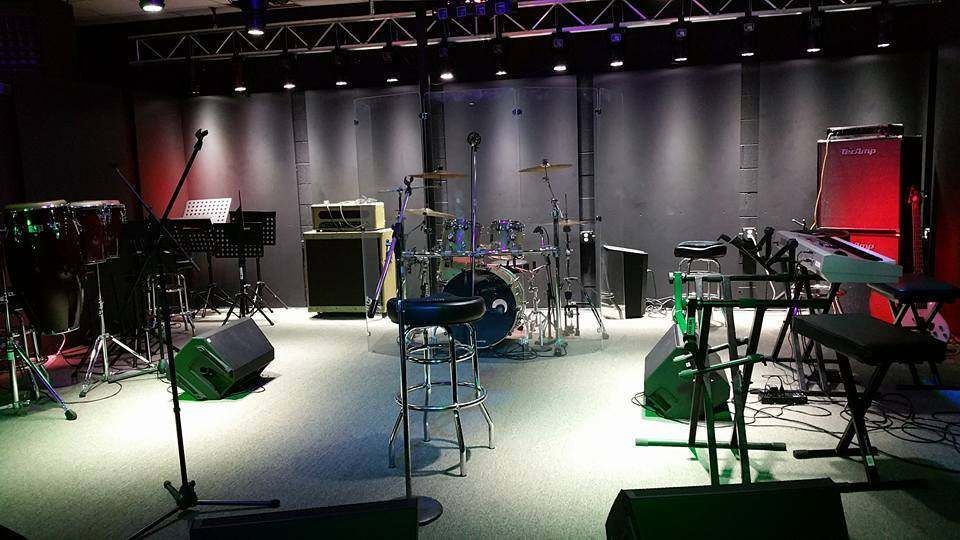 A music studio with drum set, amps, keyboards, and stage lighting, creating an empty stage.