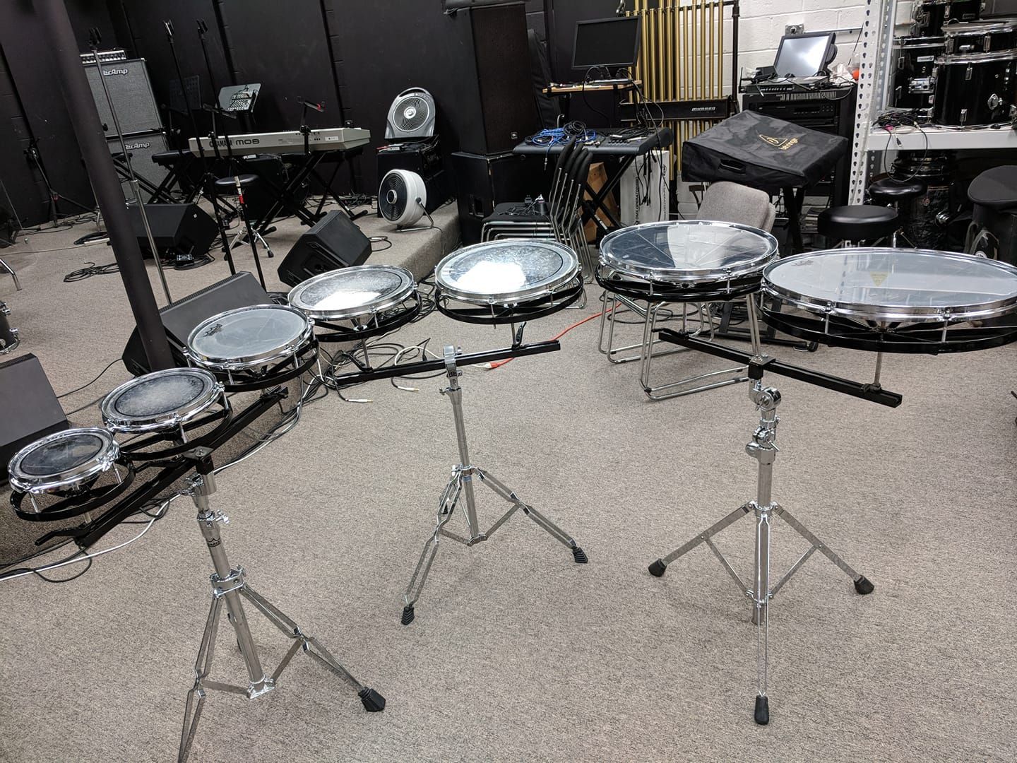 Drum set with five silver-rimmed drums on stands in a music studio setting.