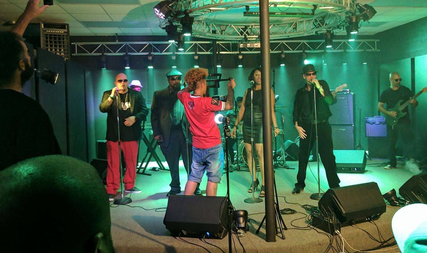 Band performing on stage, lit with green lights. Person filming them.