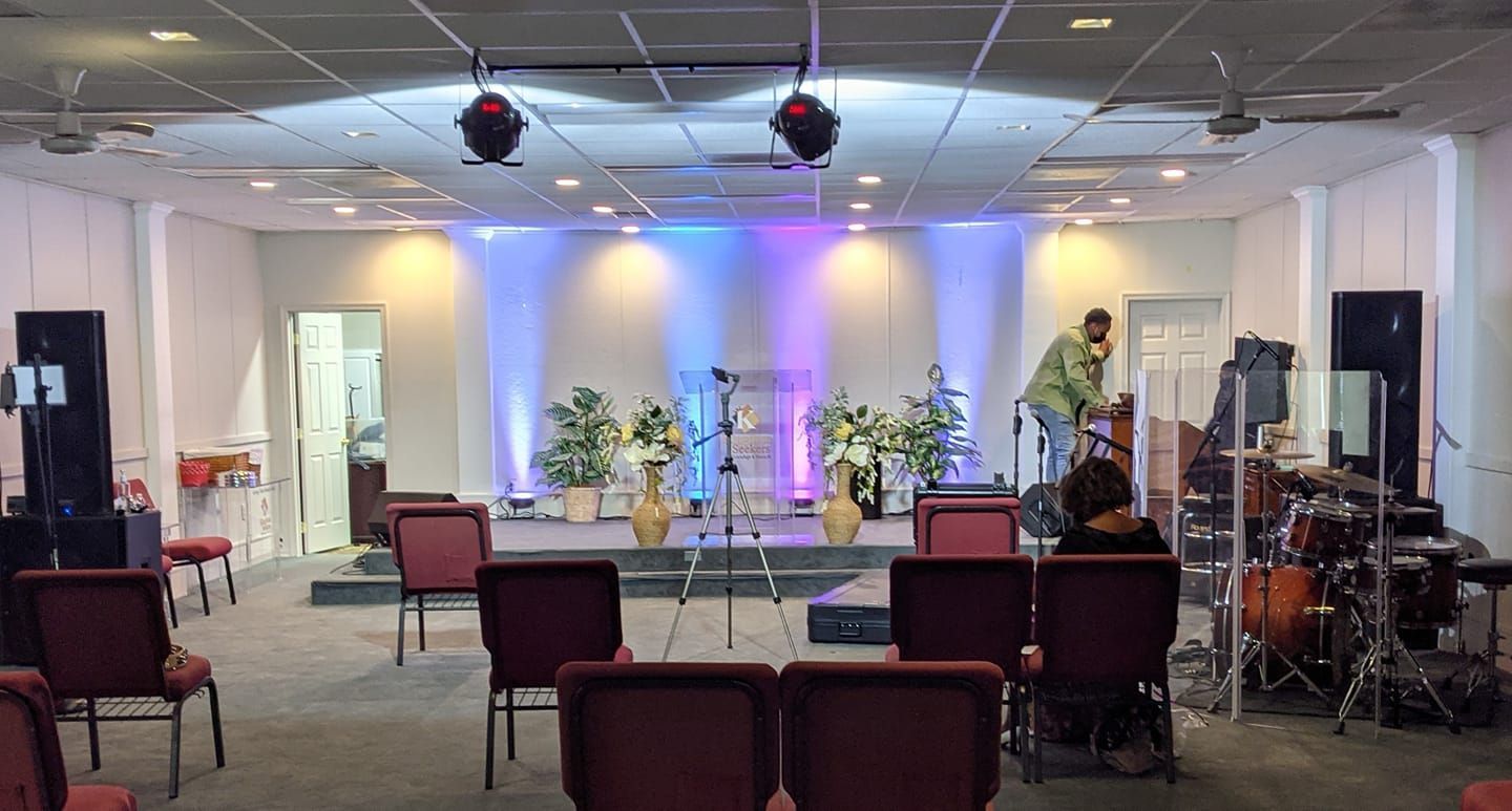 Church stage setup with lighting, flowers, and chairs; a person adjusts equipment.