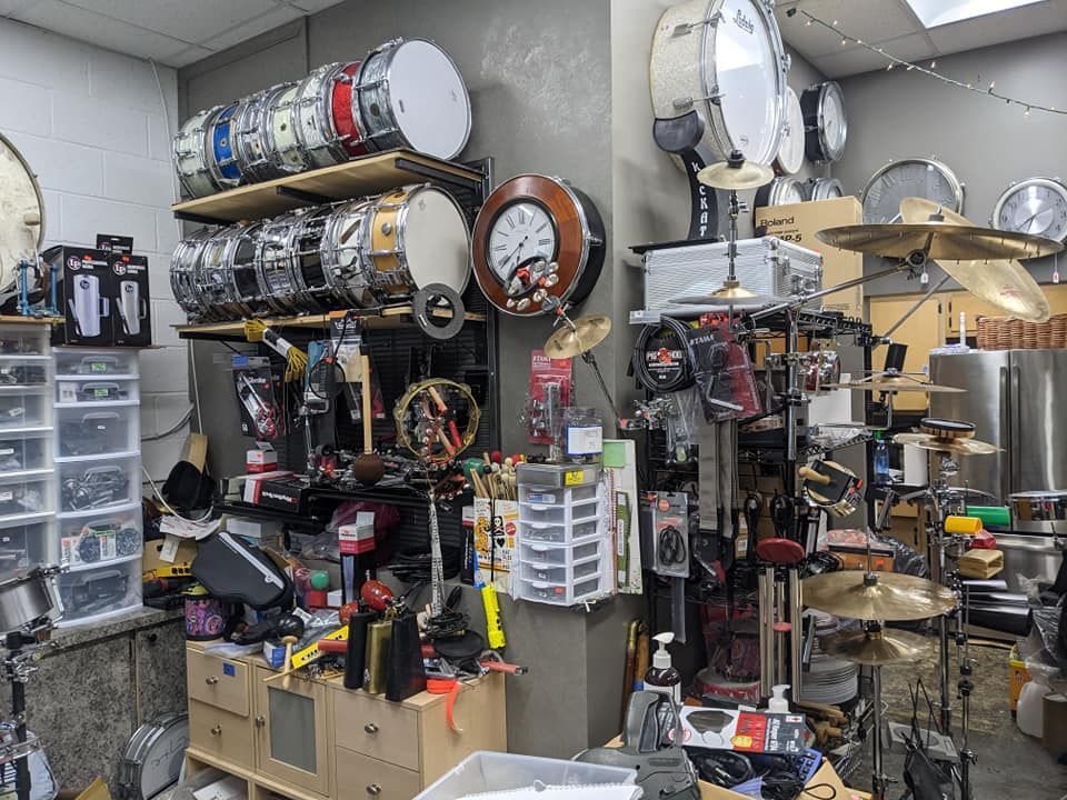 A cluttered music store with many drums, cymbals, and accessories on shelves and counters.