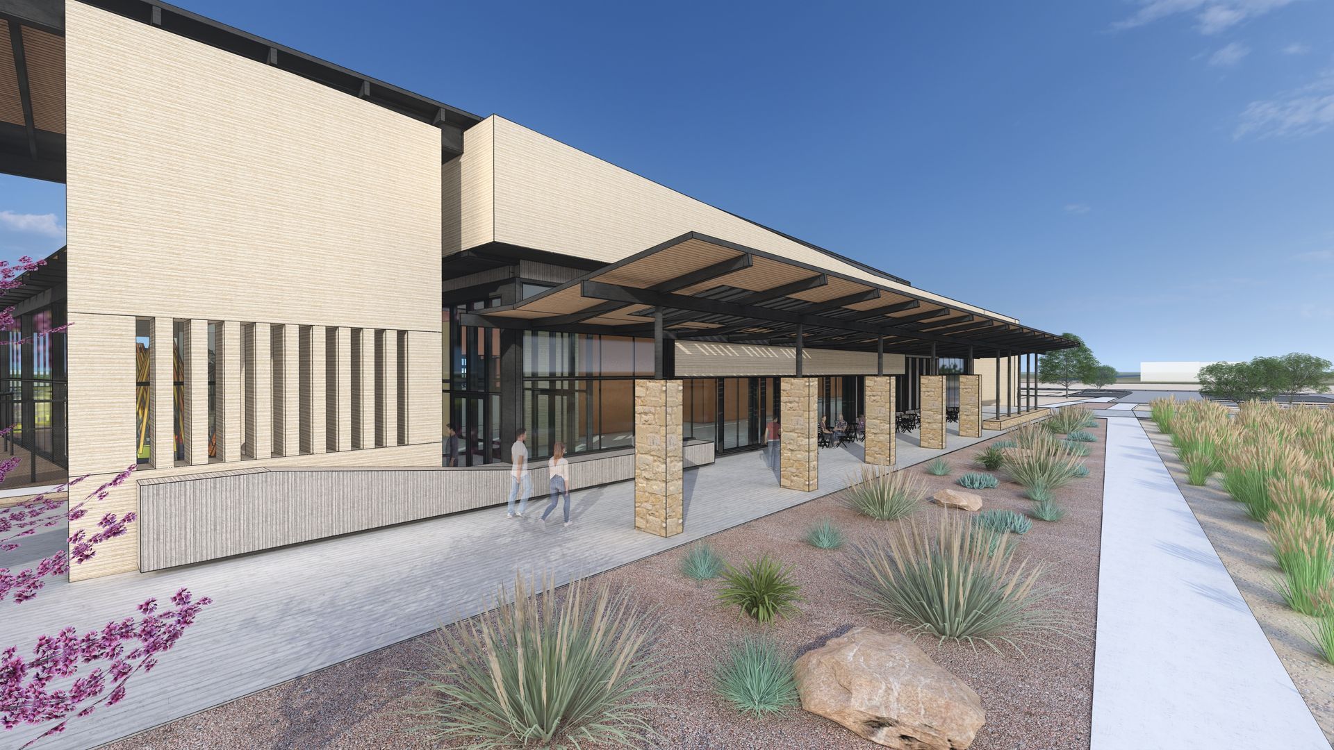 Modern building exterior with covered walkway, desert landscaping, and blue sky.