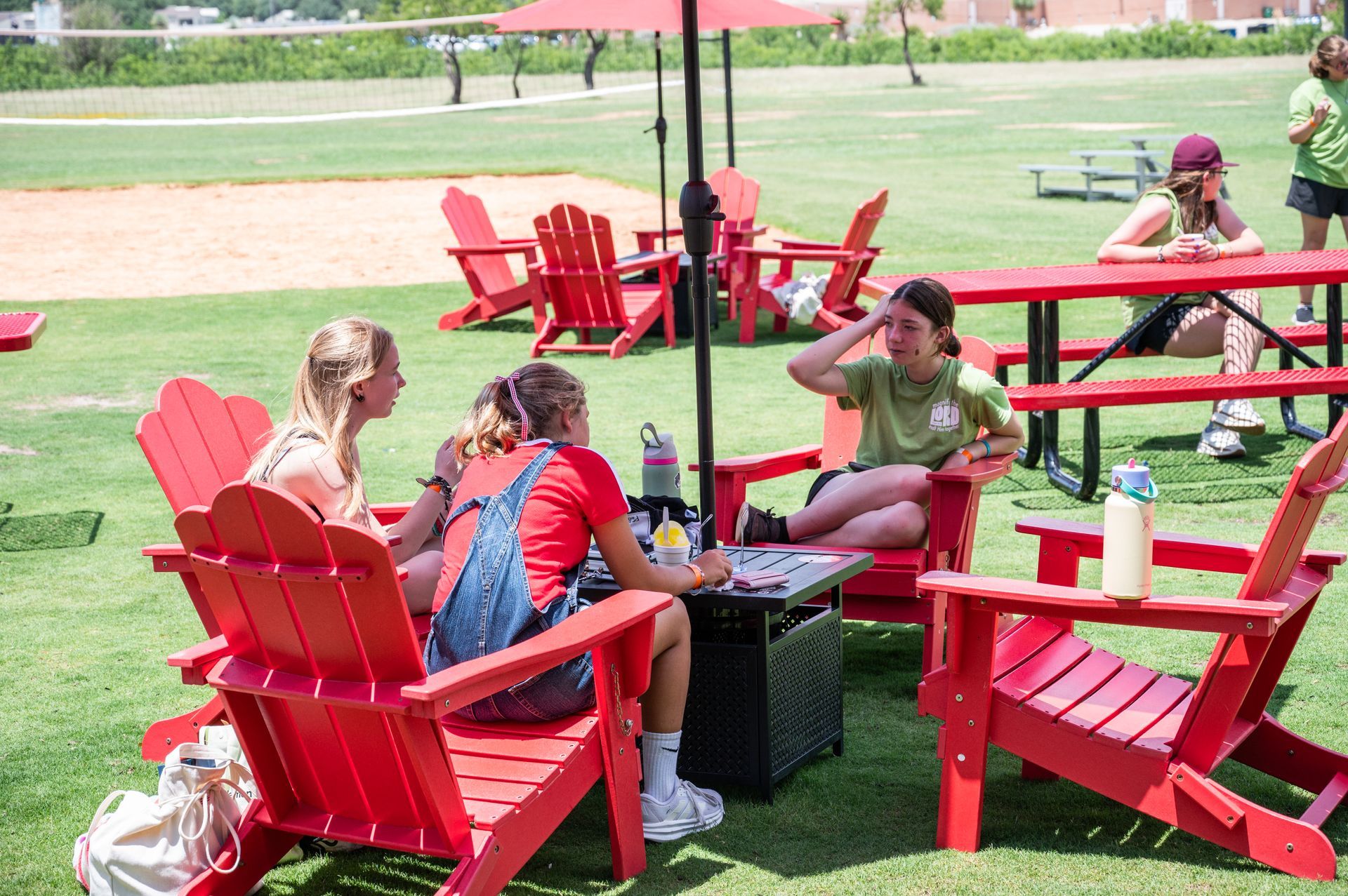 Three girls sitting in red Adirondack chairs play a game outdoors on a sunny day.